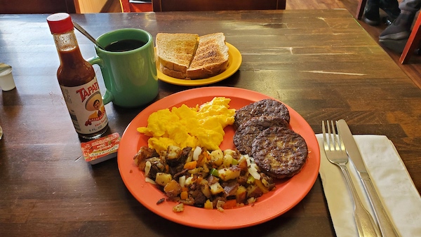 Breakfast plate with scrambled eggs, sausage patties, homefried potatoes, toast and a cup of coffee.