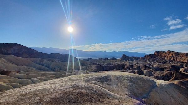 The afternoon sun and mostly blue sky over Zabriskie Point in Death Valley National Park.